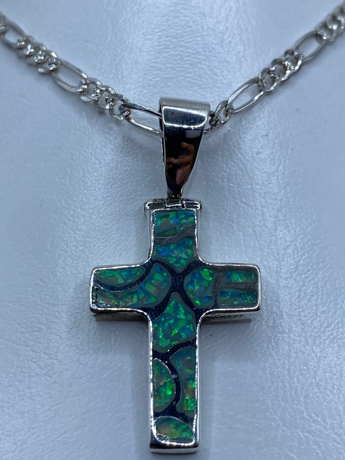 Cruz de plata con ópalo que refleja tonos verdes y azules, vista lateral