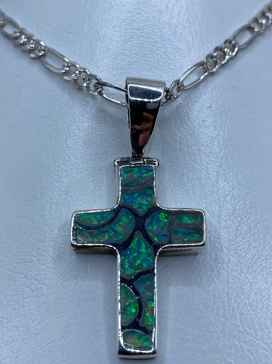 Cruz de plata con ópalo que refleja tonos verdes y azules, vista lateral