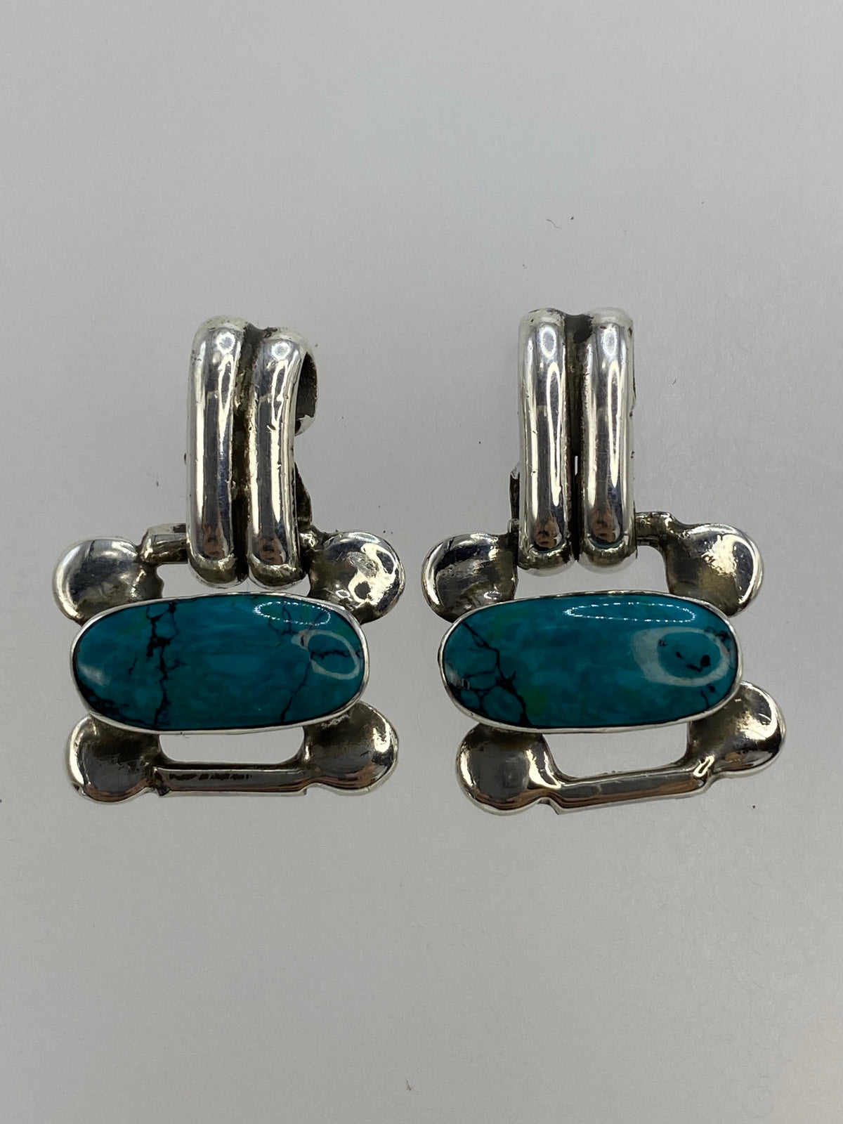 Par de aretes de plata con turquesa azul engastada, forma de hueso, sobre fondo blanco