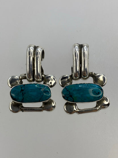 Par de aretes de plata con turquesa azul engastada, forma de hueso, sobre fondo blanco