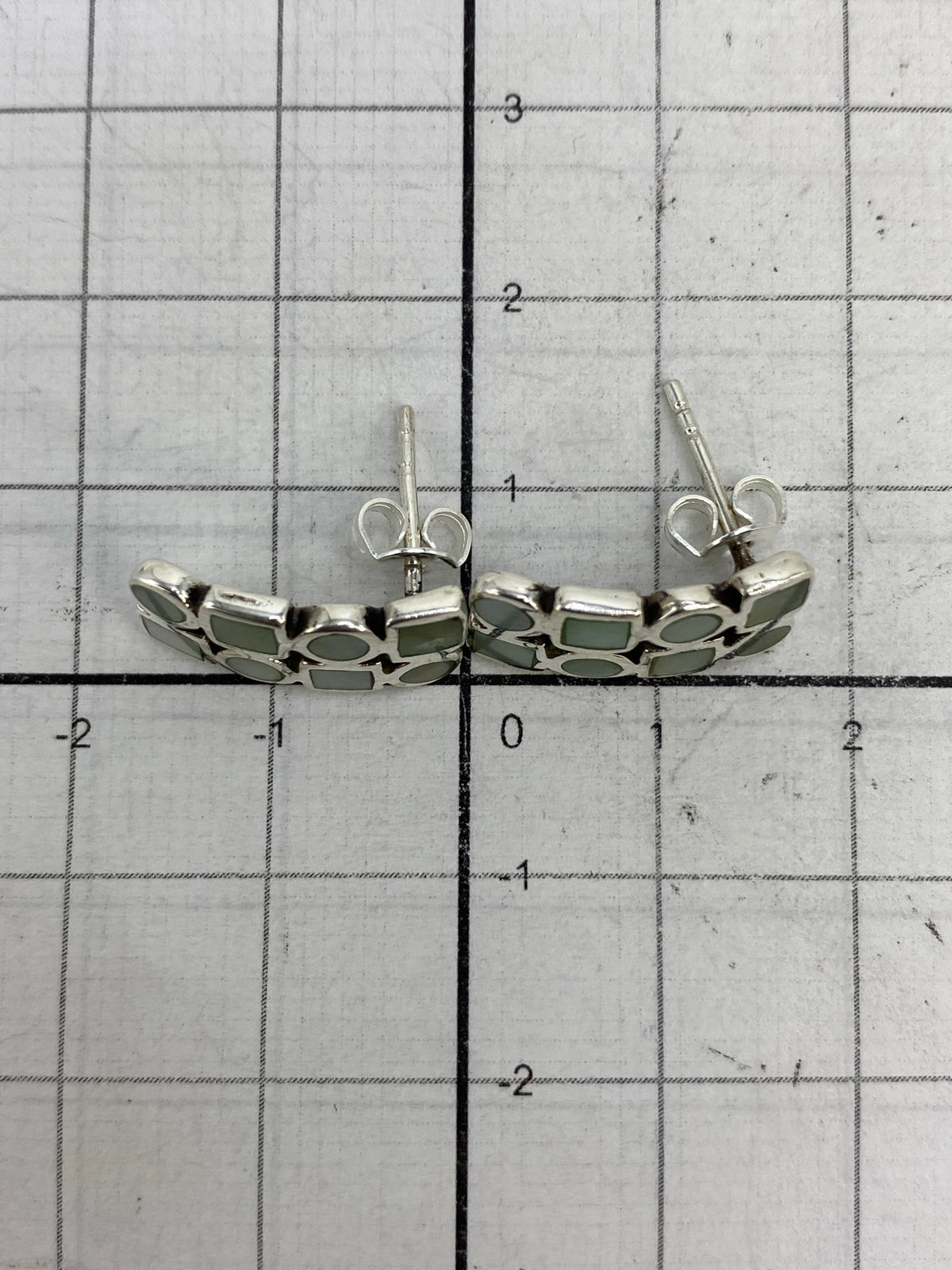 Aretes sobre fondo blanco, escala al lado mostrando tamaño real de 1.5 cm