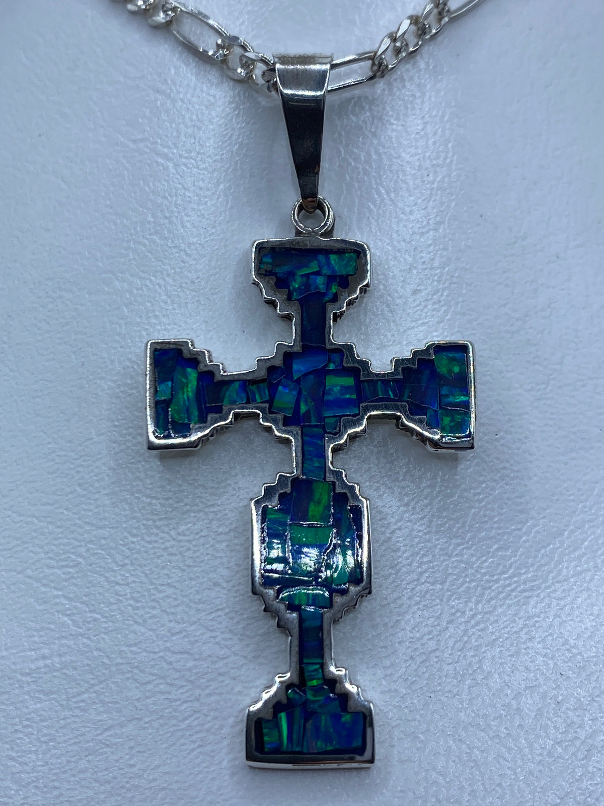 Dije cruz de plata 950 con ópalo de fuego azul engastado, visto de frente con reflejos azules y verdes