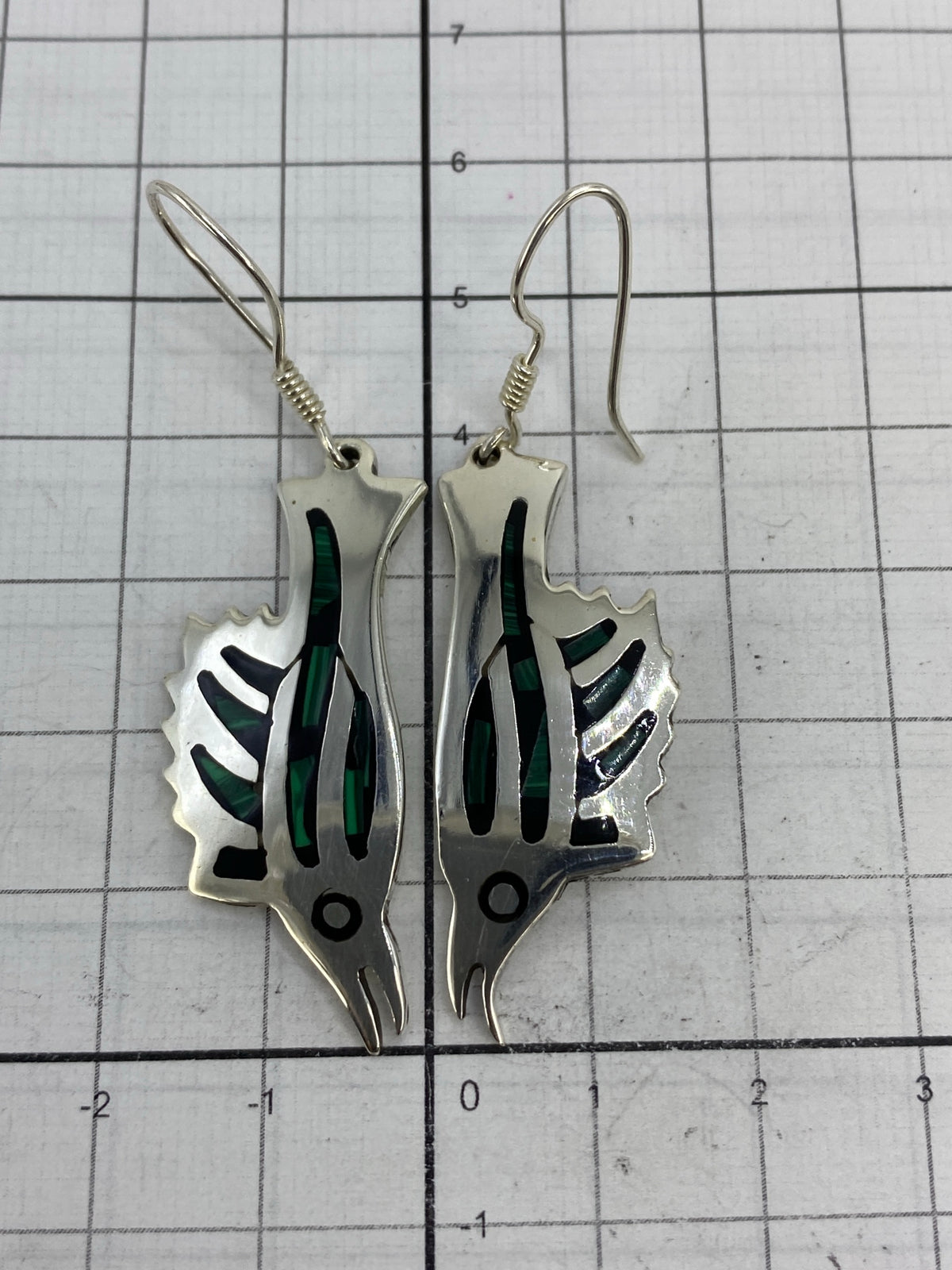 Aretes de plata sobre regla de centímetros mostrando el largo de 5.7 cm y ancho de 1.5 cm