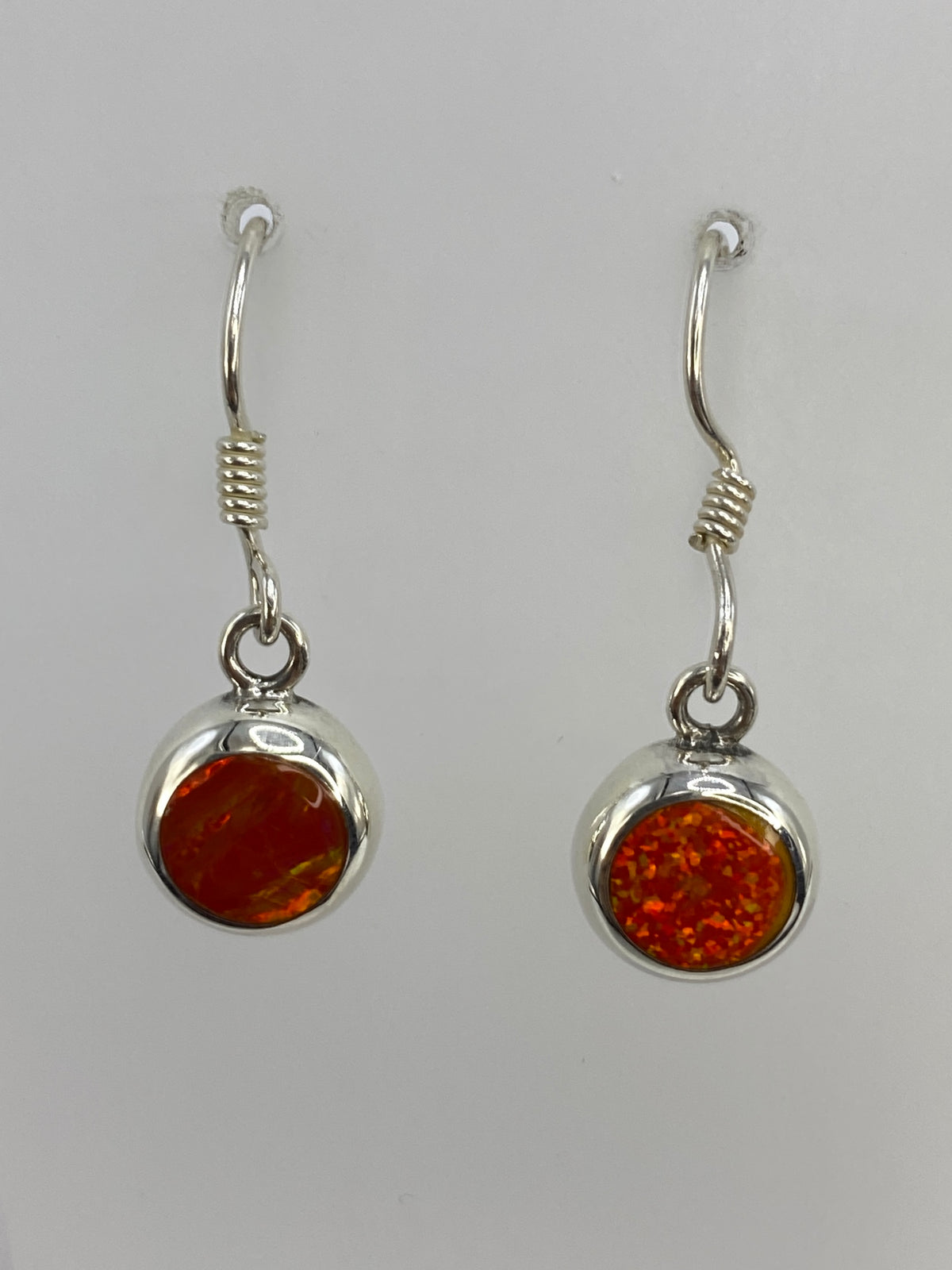Dos aretes colgando del gancho de plata, mostrando el brillo del ópalo de fuego