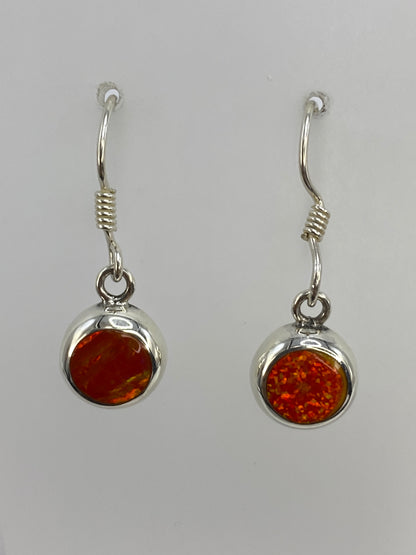 Dos aretes colgando del gancho de plata, mostrando el brillo del ópalo de fuego