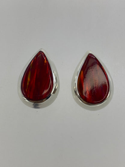 Detalle frontal de los aretes mostrando el rojo profundo y los destellos del ópalo