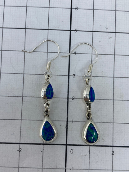 Aretes de plata sobre fondo azul, mostrando destellos verdes del ópalo de fuego