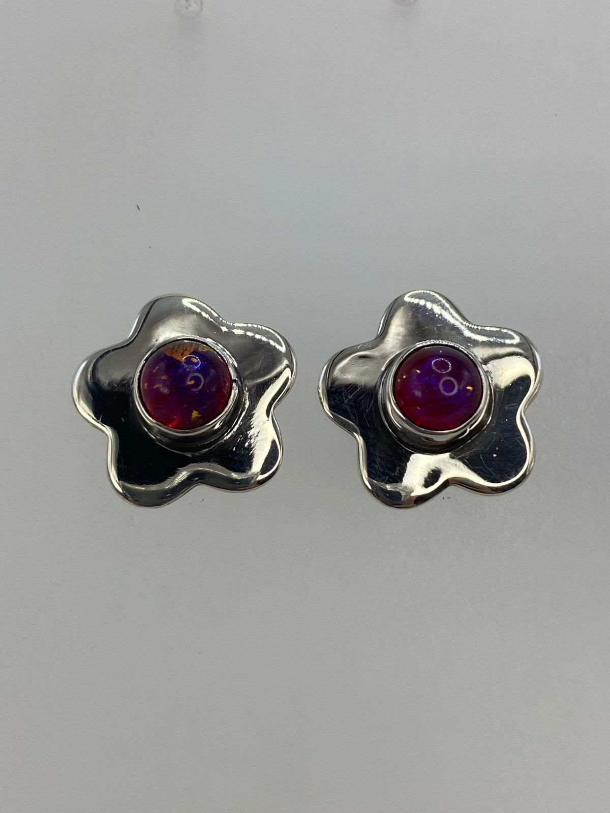 Vista frontal de aretes de plata con incrustación de piedra morada, sobre fondo gris