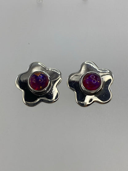 Vista frontal de aretes de plata con incrustación de piedra morada, sobre fondo gris