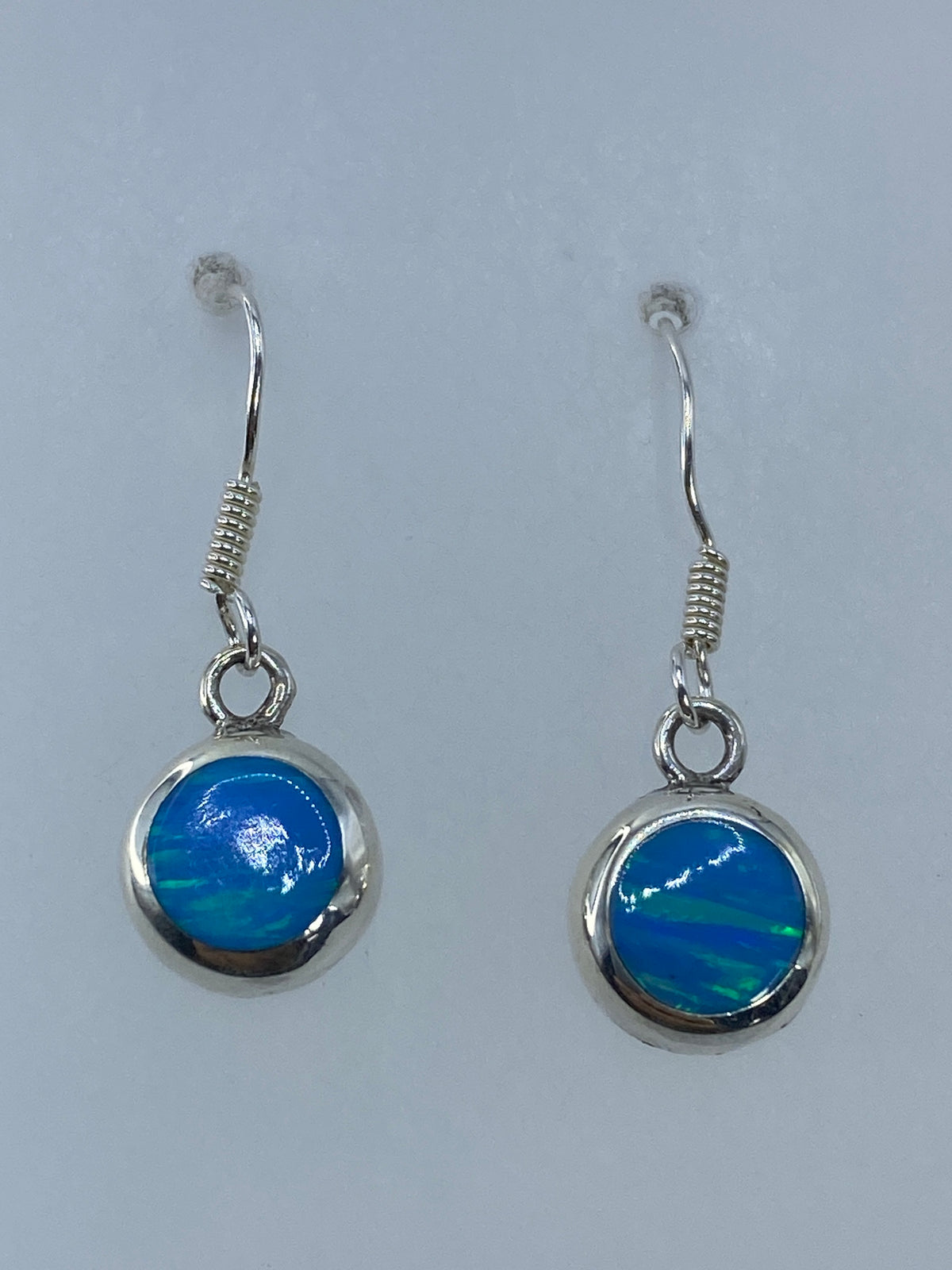 Arete individual colgando, mostrando el ópalo de fuego con destellos verdes y azules