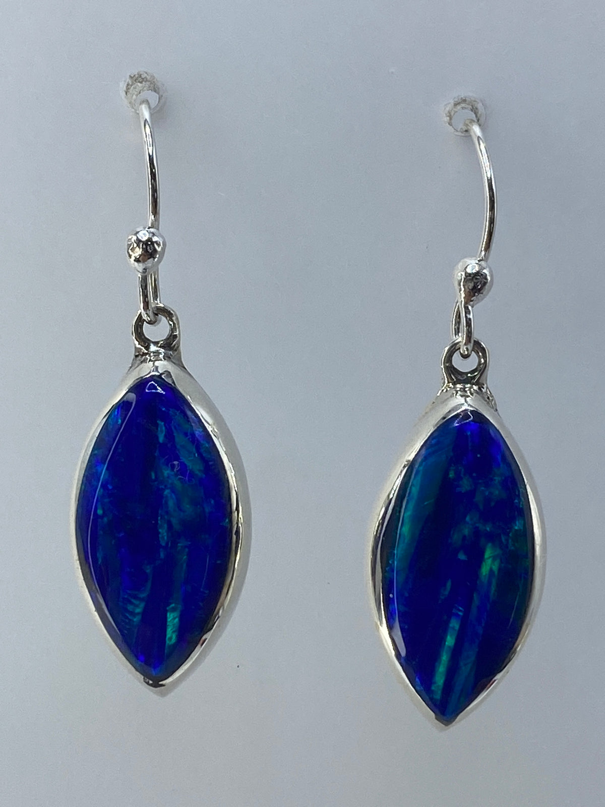 Par de aretes de plata con ópalo de fuego verde olivo, colgando de ganchos de plata, sobre fondo gris