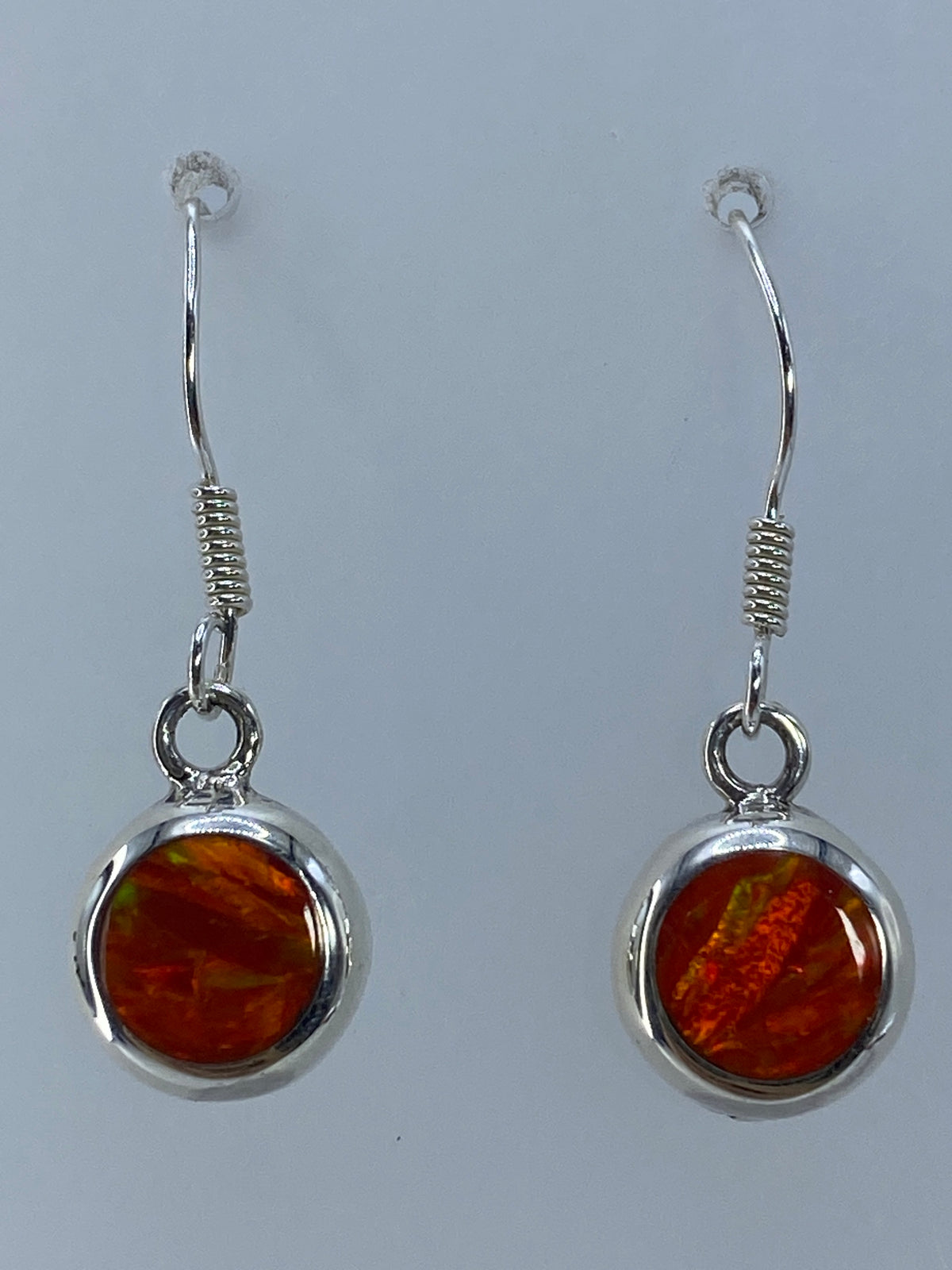 Par de aretes de plata 925 con ópalo de fuego naranja, colgando contra fondo neutro