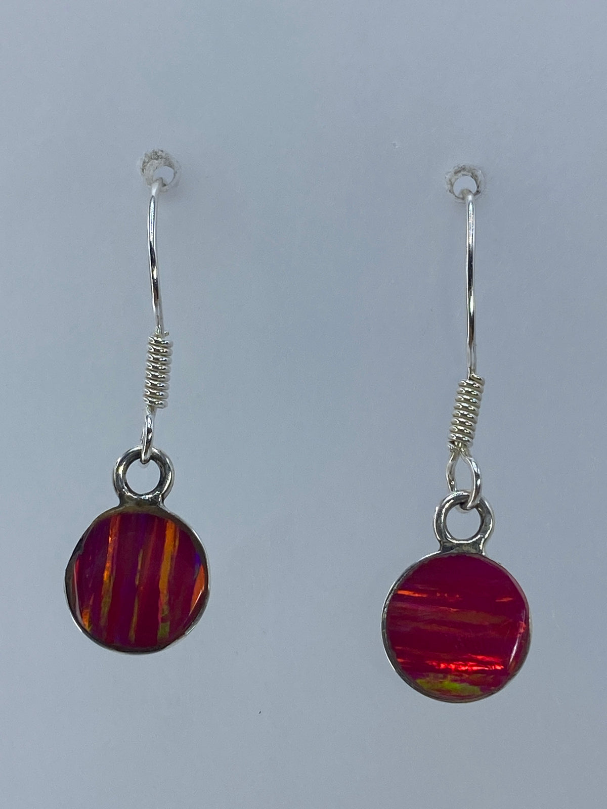 Par de aretes de plata con ópalo de fuego rosa engastado, colgando sobre fondo blanco