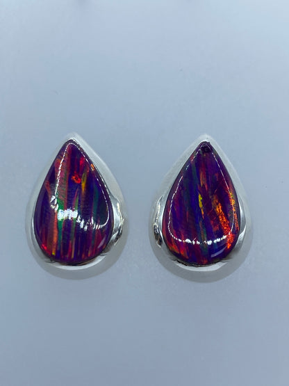 Vista frontal de los aretes de ópalo morado engastados en plata, sobre fondo gris