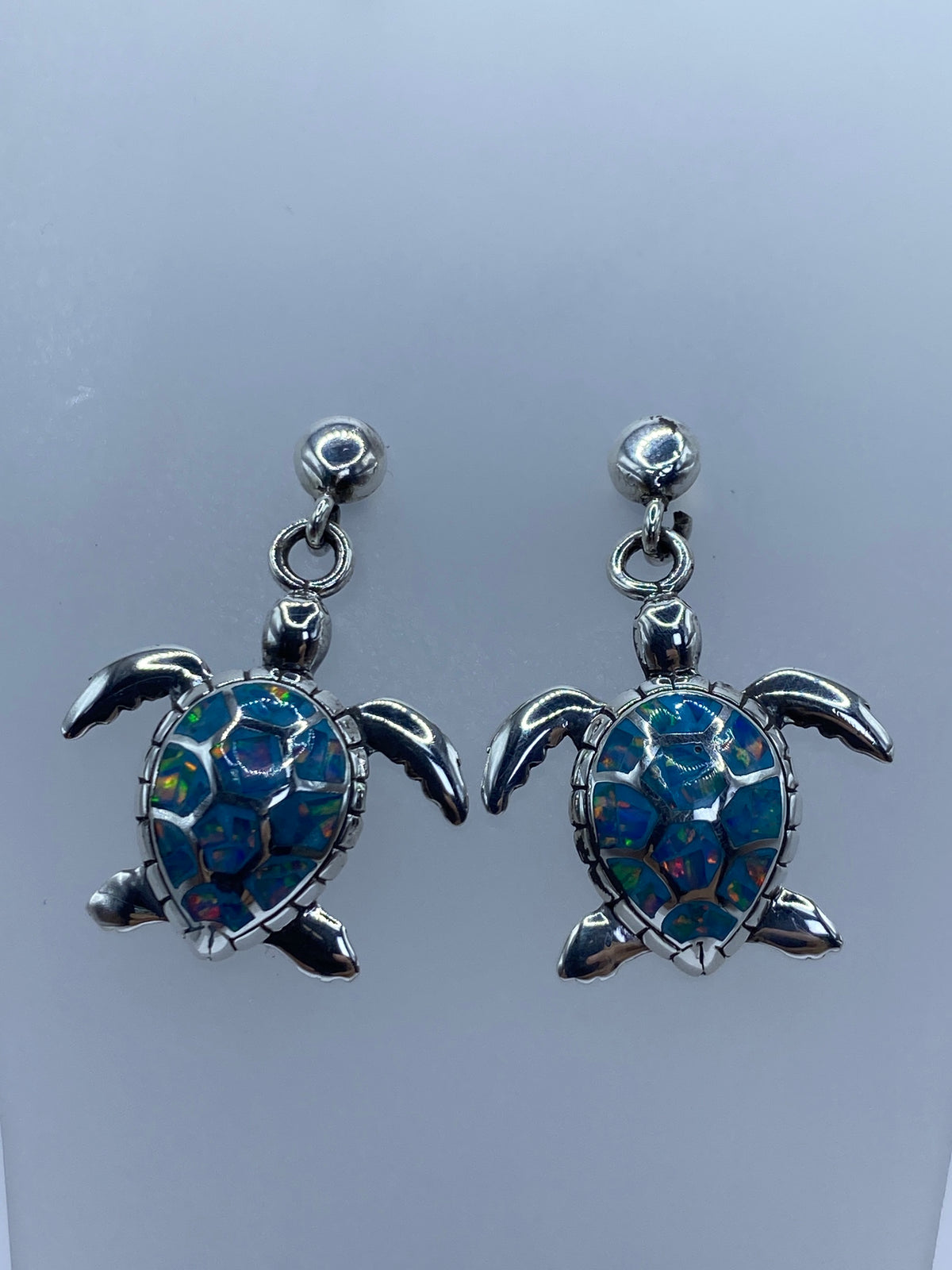 Arete individual de tortuga marina con ópalo multicolor mostrando el engaste a mano
