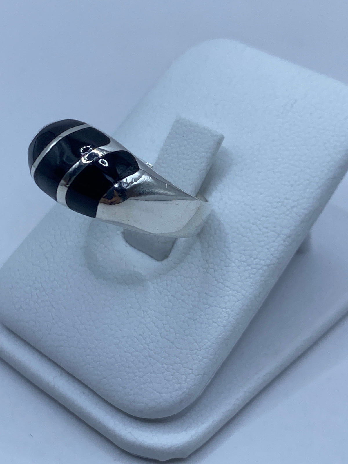 Anillo de plata engastado con ónix negro en la mano de una persona, lado frontal
