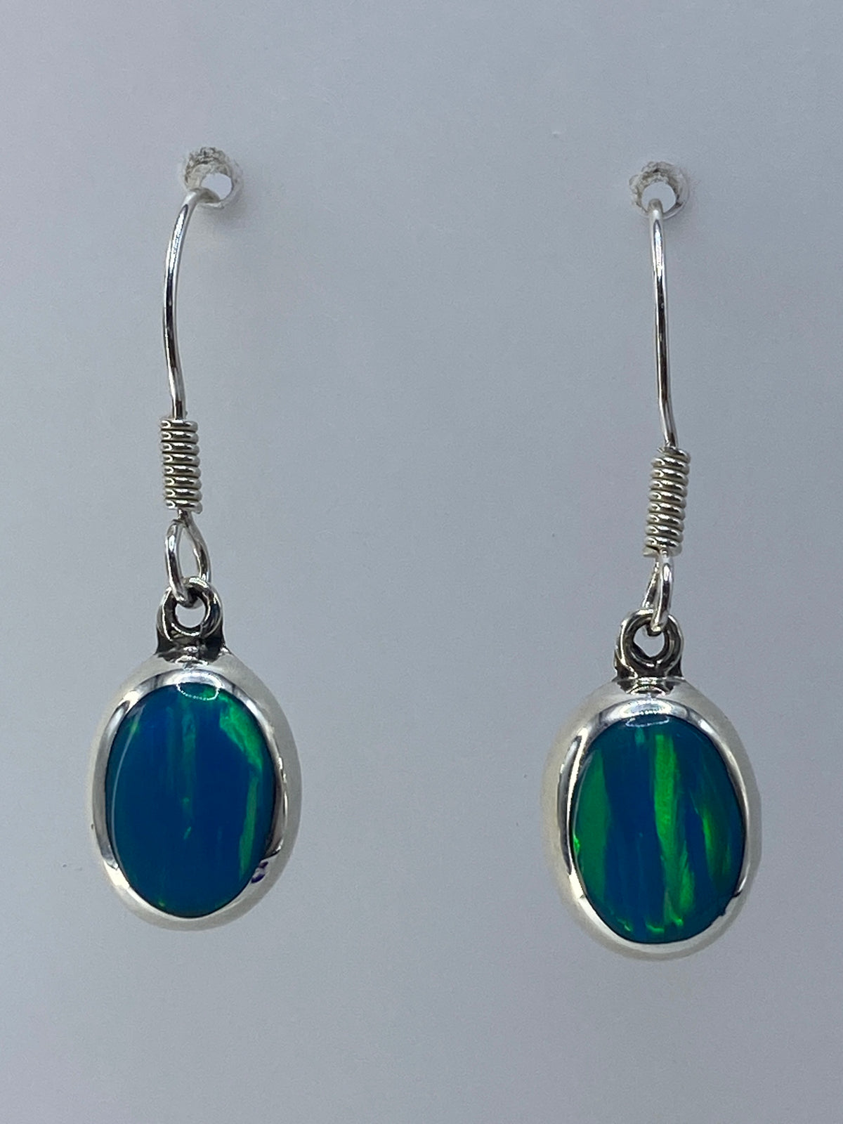 Detalle de los aretes mostrando el ópalo de fuego con sus tonos verdes y azulados engastado en plata