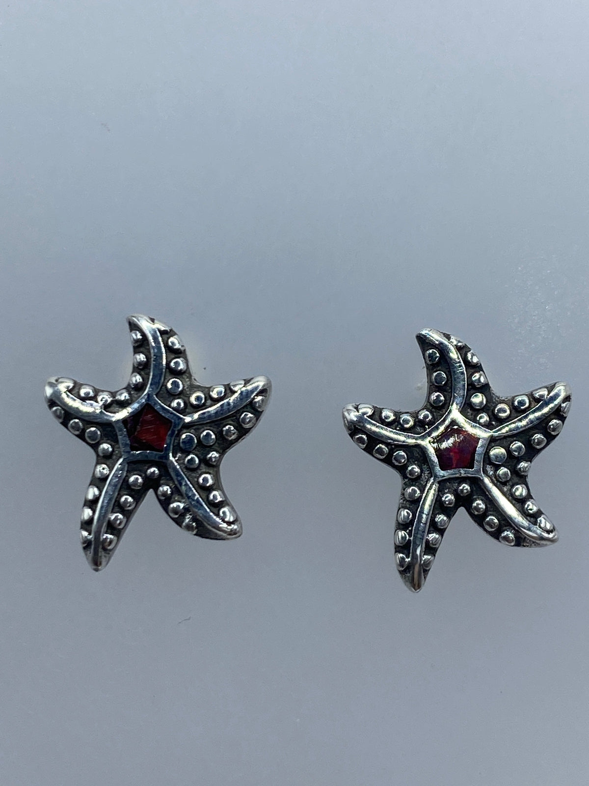 Aretes de tamaño miniatura (1.4 cm) sobre regla de centímetros, con poste y mariposa visible