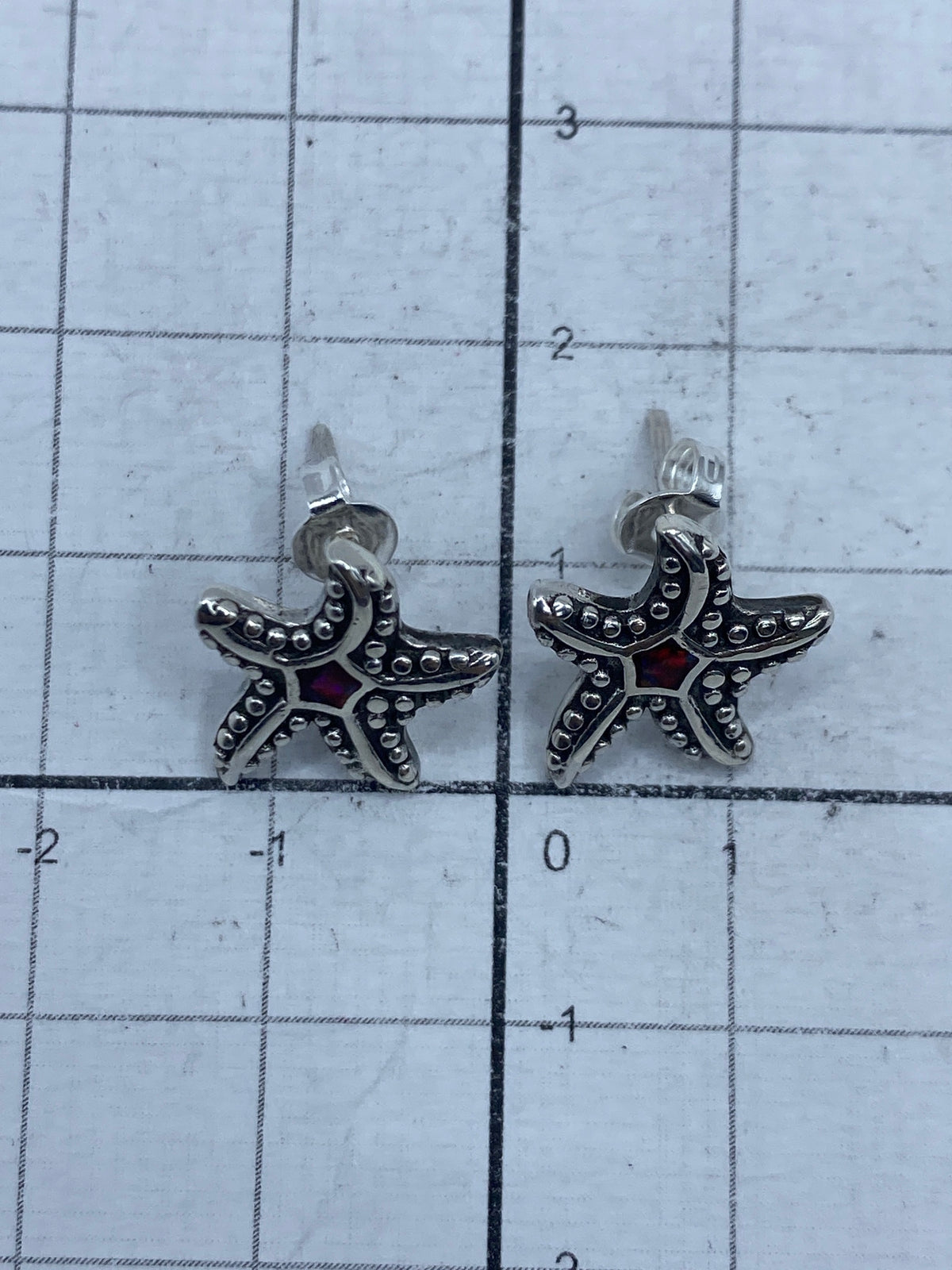 Par de aretes con ópalo de fuego rojo en mano, mostrando el brillo y color del acabado