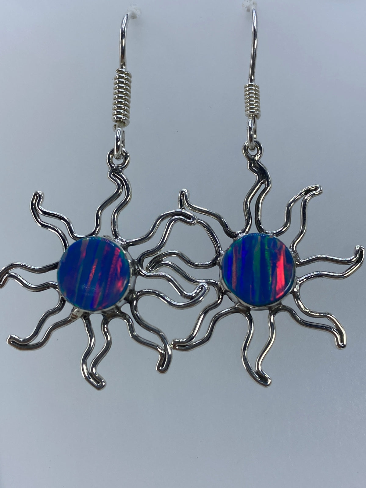 Par de aretes de plata con ópalo de fuego multicolor colgando, mostrando los destellos azul, rojo y verde de la piedra