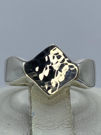 Anillo de plata repujada con motivo geométrico en relieve, visto de frente sobre fondo gris