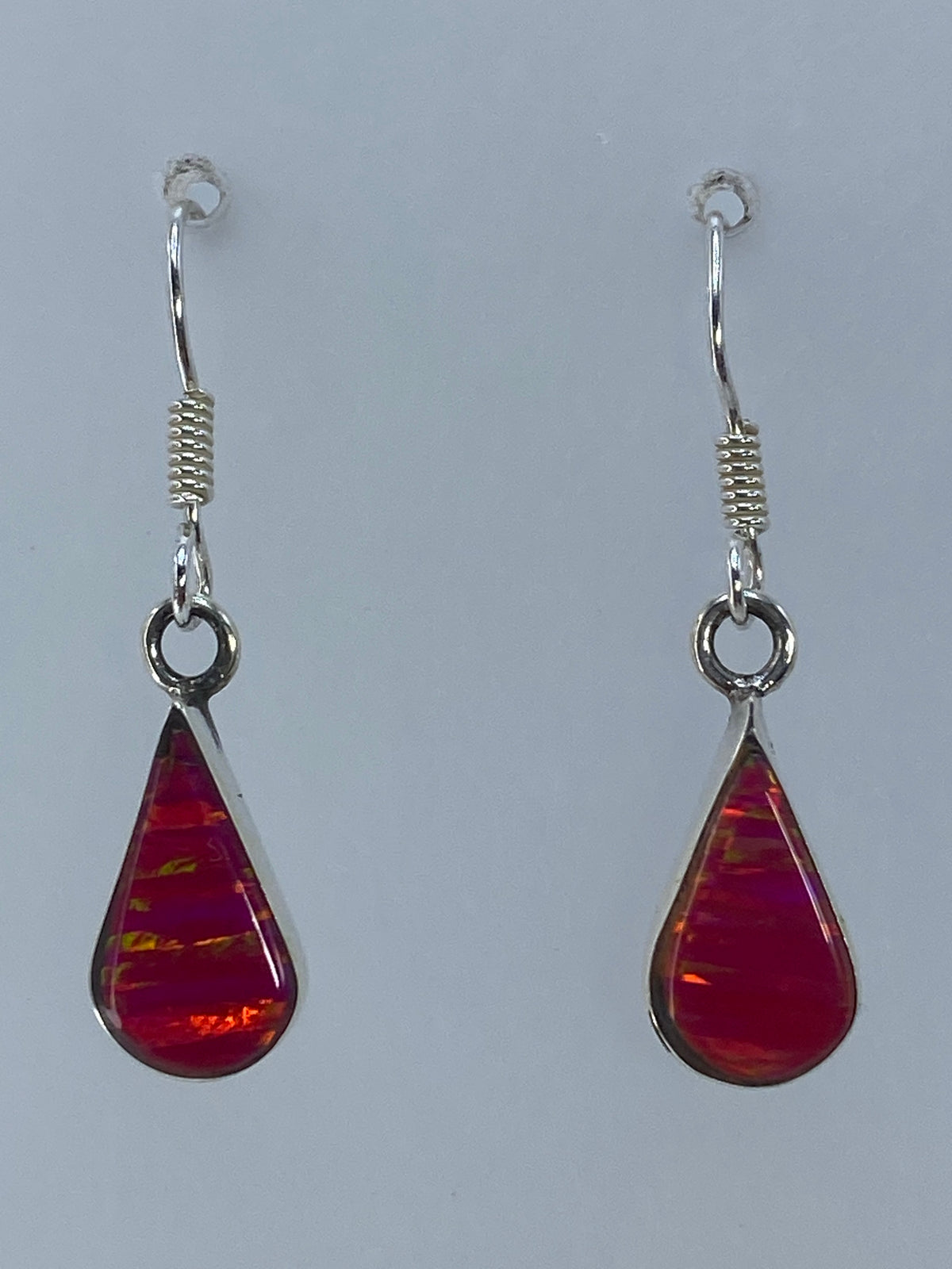 Par de aretes de plata 950 con ópalo de fuego rosa colgando sobre fondo neutro