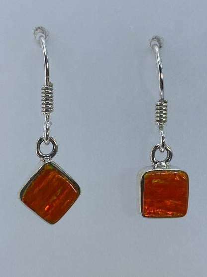 Par de aretes de plata con ópalo de fuego naranja, largos 2.8 cm, en vista frontal sobre fondo gris