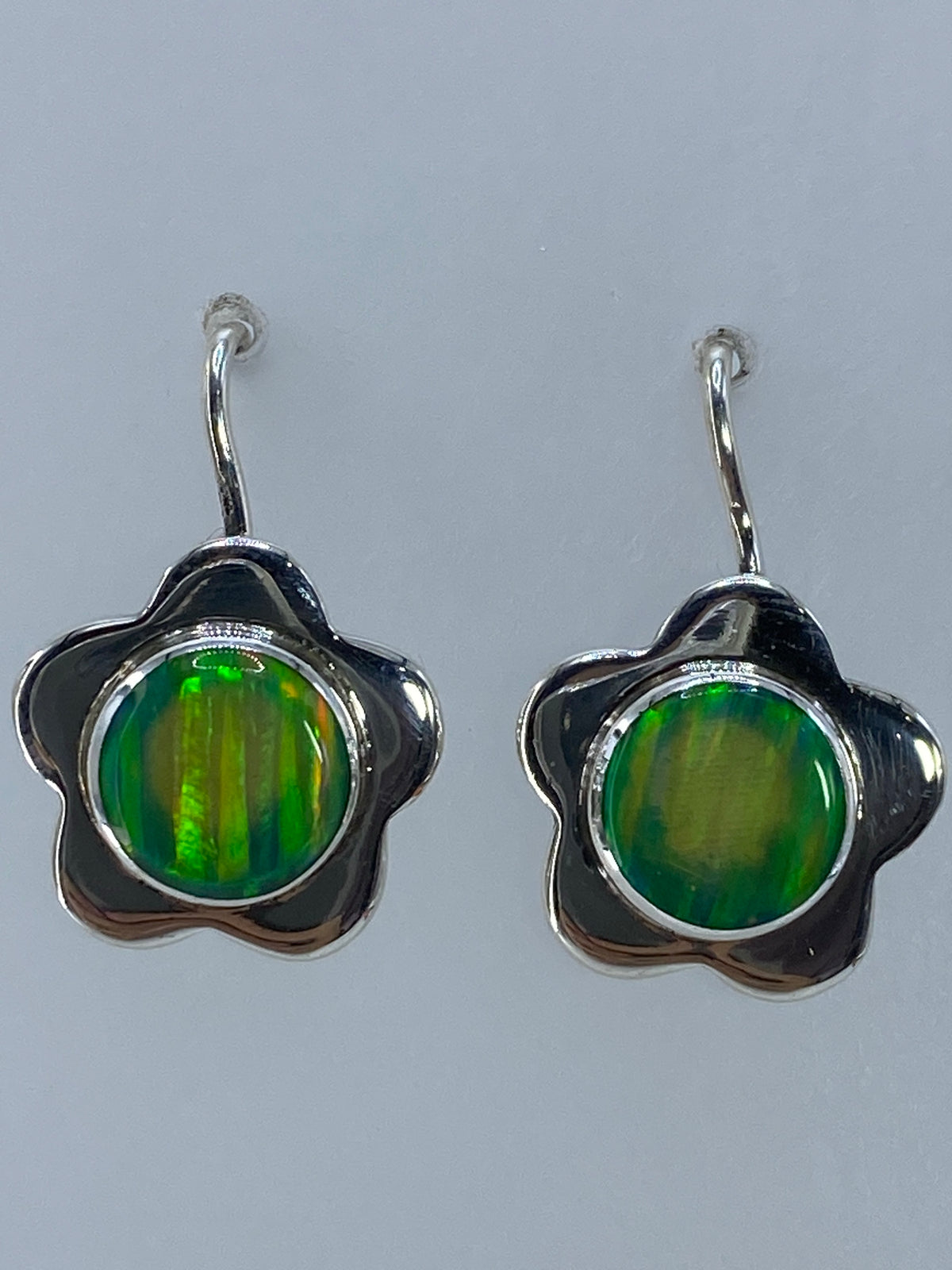 Aretes colgando contra fondo blanco mostrando el brillo verde limón del ópalo
