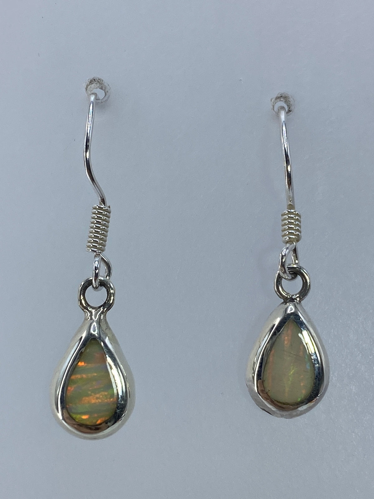 Par de aretes de plata con ópalo de fuego multicolor colgando, vista frontal