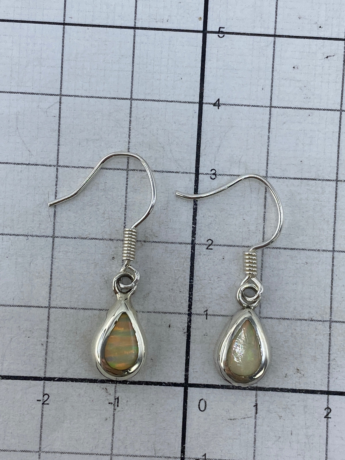 Aretes de plata pura colgando, mostrando el largo de 3 cm y el engaste a mano del ópalo