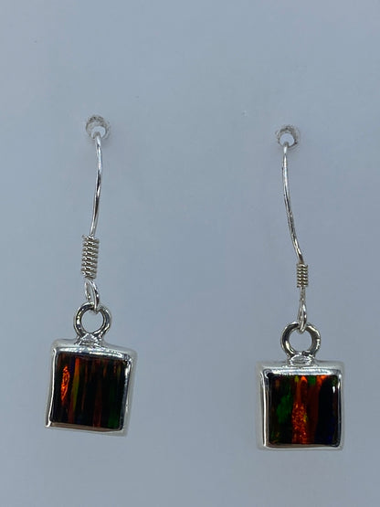 Aretes de plata con ópalo de fuego multicolor colgando de un par de orejas