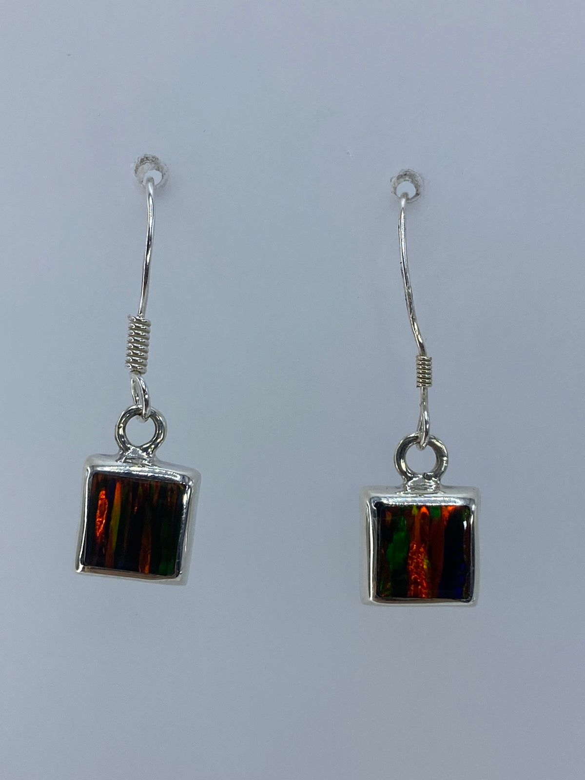 Detalle frontal de los dos aretes mostrando el ópalo de fuego con destellos rojos y verdes