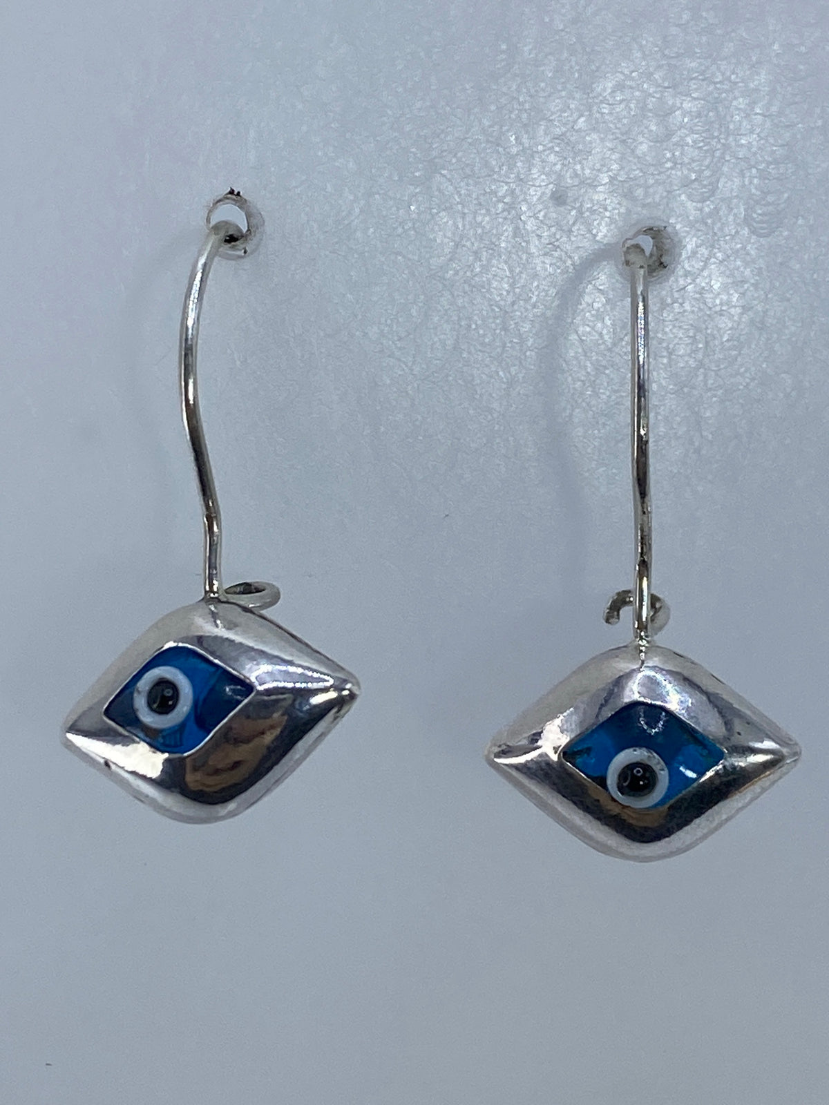 Par de aretes de plata con ojo protector azul cielo, colgando de gancho de plata