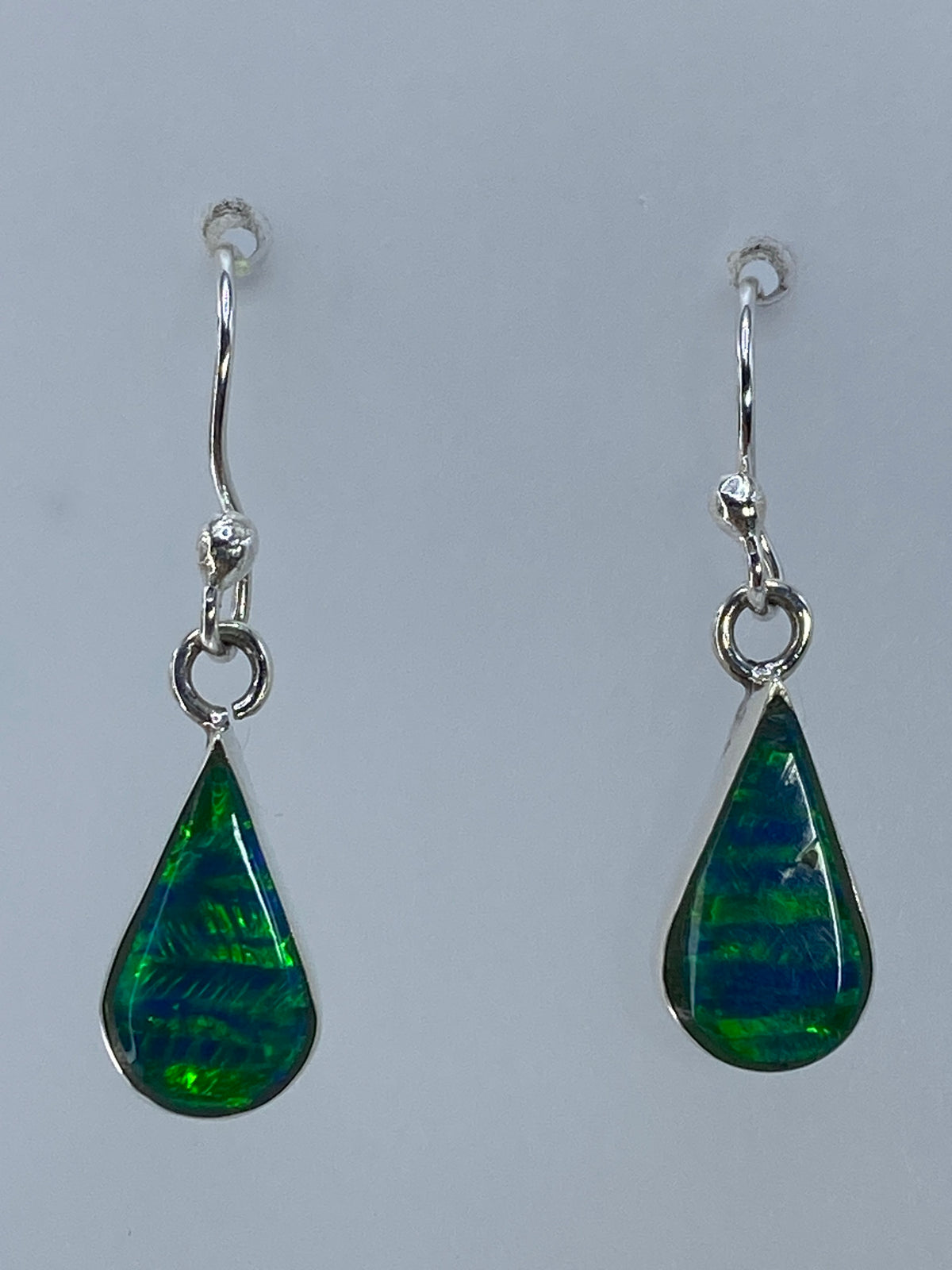 Par de aretes de plata 950 con ópalo de fuego verde engastado, sobre medidor de centímetros mostrando 2.7 cm de largo