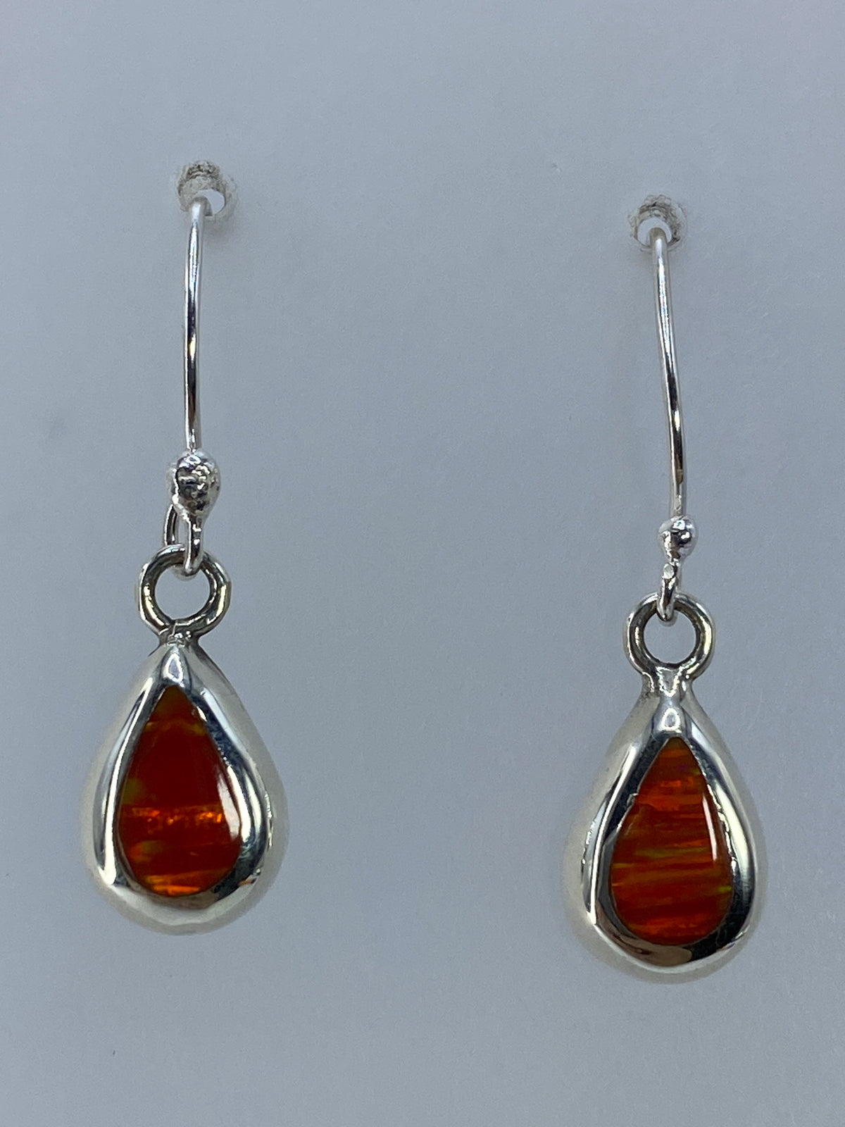 Par de aretes de plata con ópalo de fuego naranja engastado, colgando sobre fondo gris