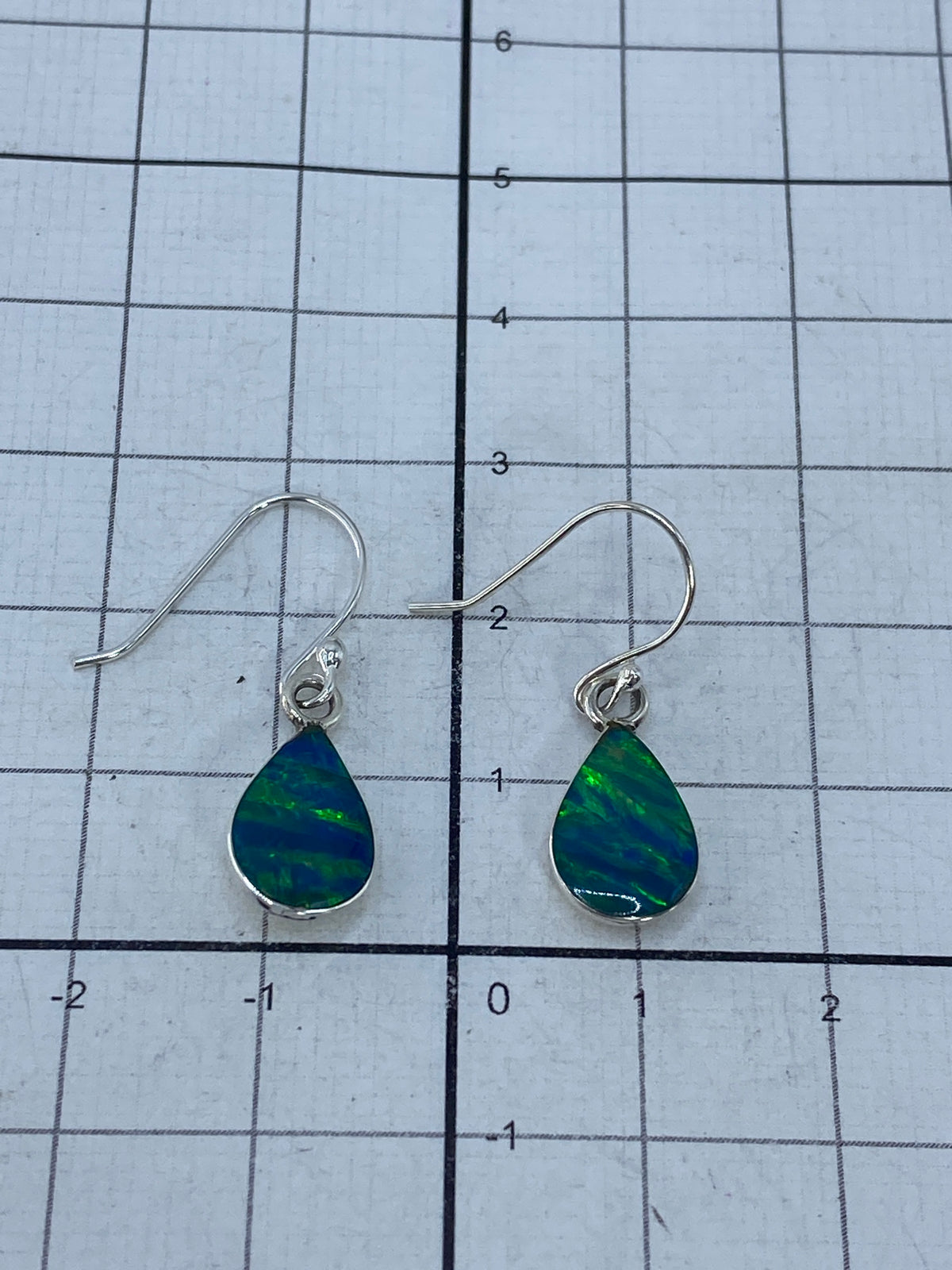 Aretes de plata con opalo de fuego sobre fondo azul, mostrando el brillo natural del opalo verde limon