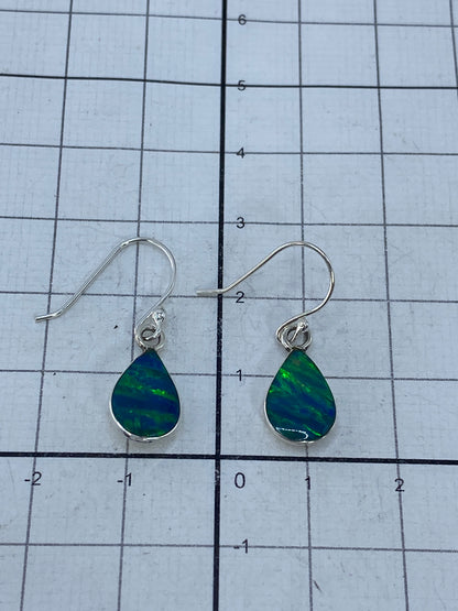 Aretes de plata con opalo de fuego sobre fondo azul, mostrando el brillo natural del opalo verde limon
