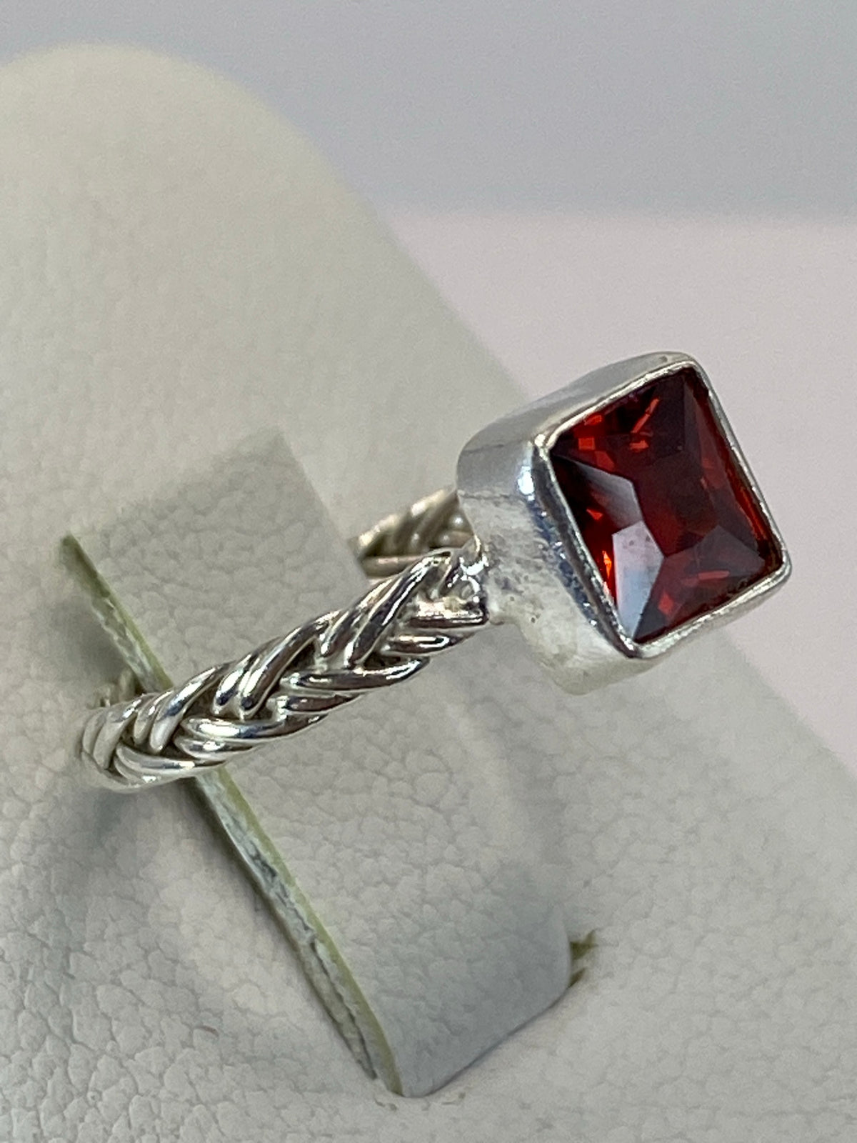 Anillo de plata trenzada con circonia roja brillante en la mano