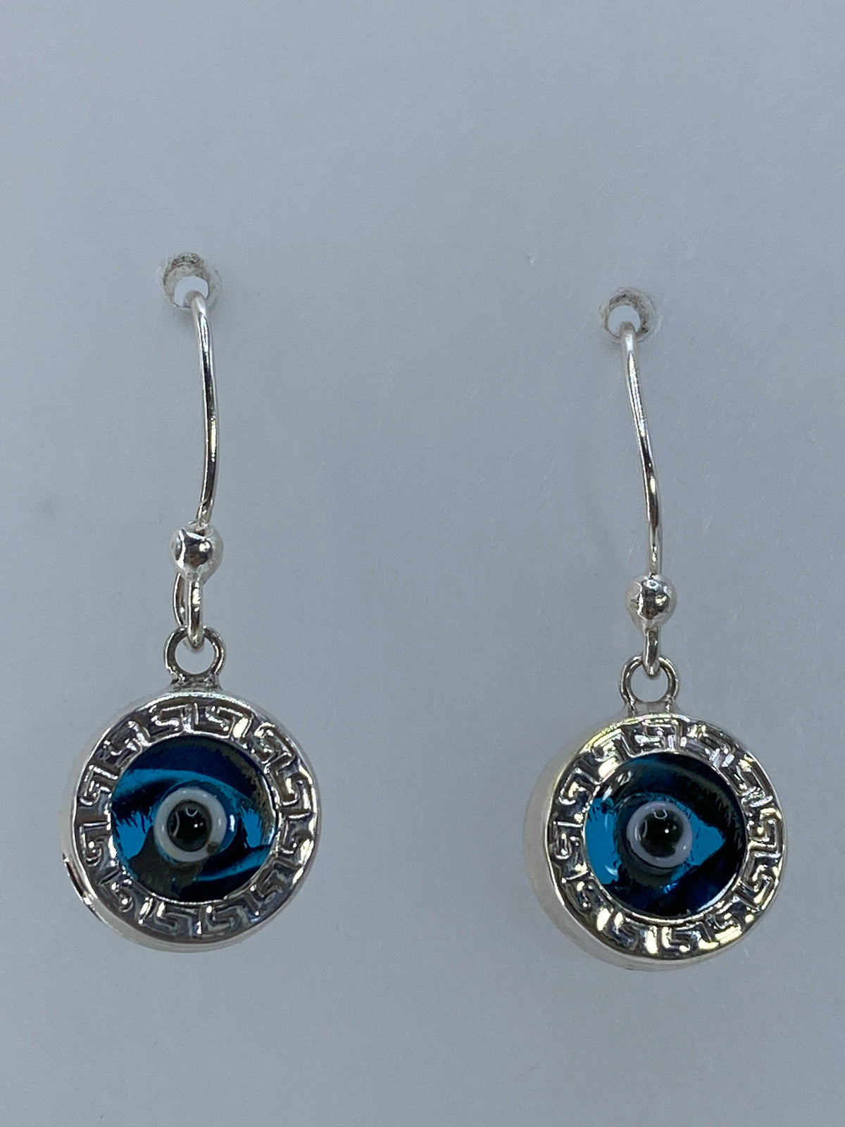 Aretes de plata con ojo azul y marco geométrico de Taxco, fotografiados frente a fondo blanco