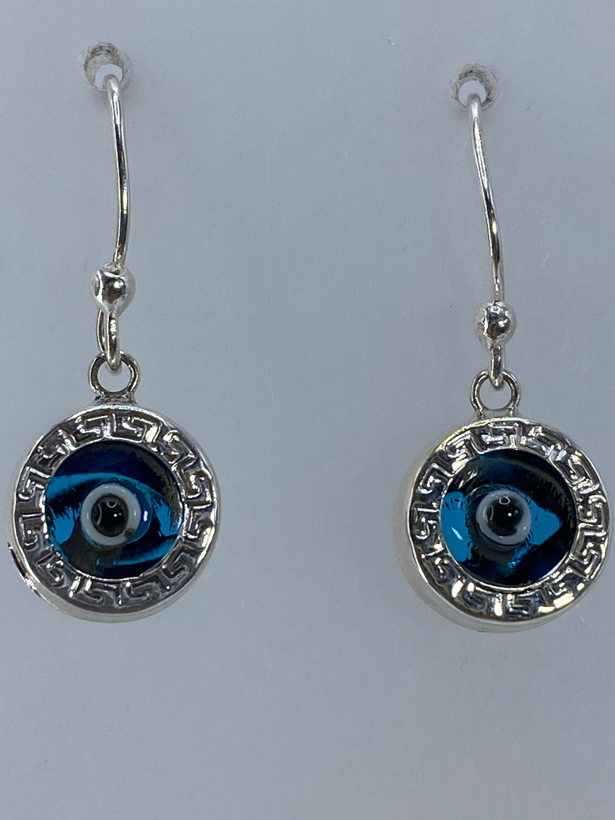 Par de aretes colgando de ganchos plateados, mostrando el diseño circular con greca
