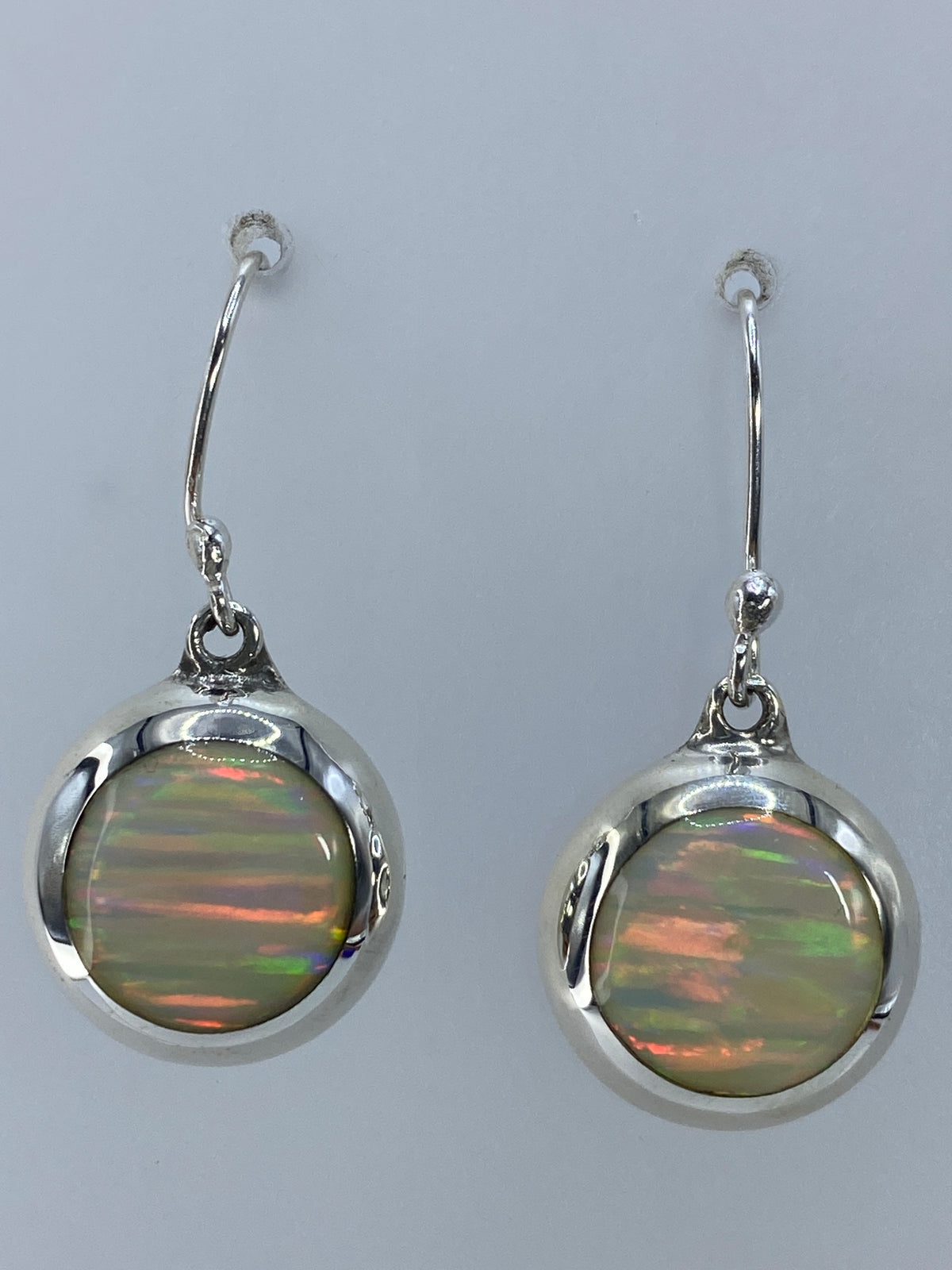 Par de aretes de plata 925 con ópalo de fuego multicolor, colgando sobre fondo gris
