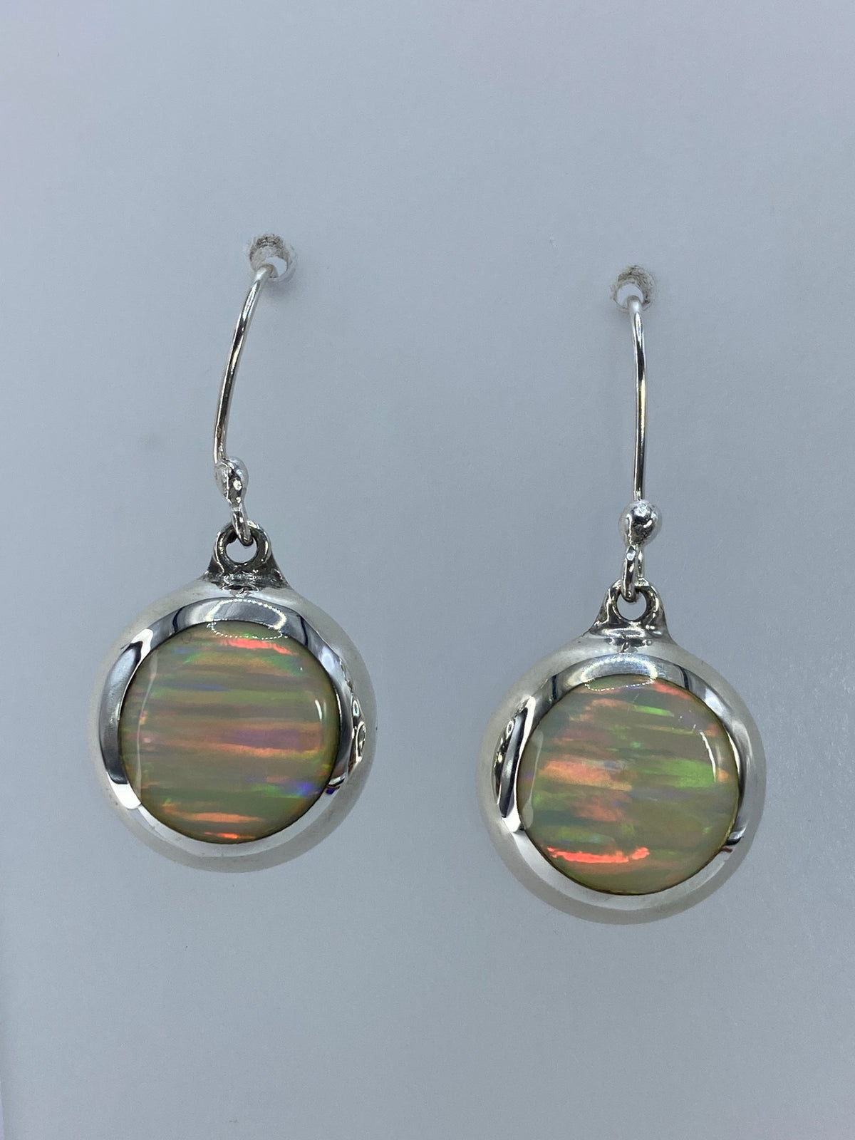 Detalle frontal de los aretes mostrando los destellos naranja, rojo y verde del ópalo
