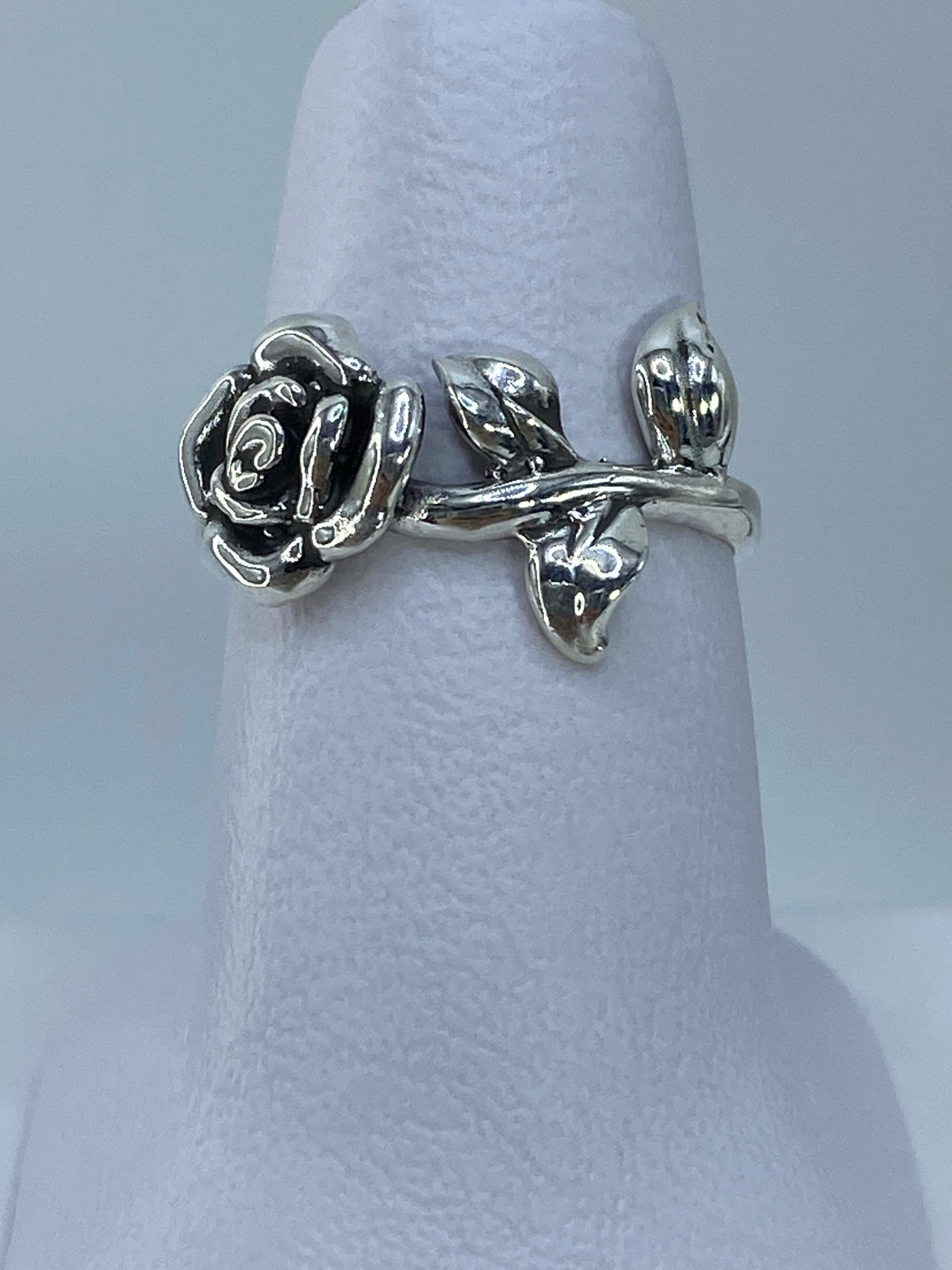 Anillo de plata repujado con rosa floral en relieve, visto de frente sobre fondo gris