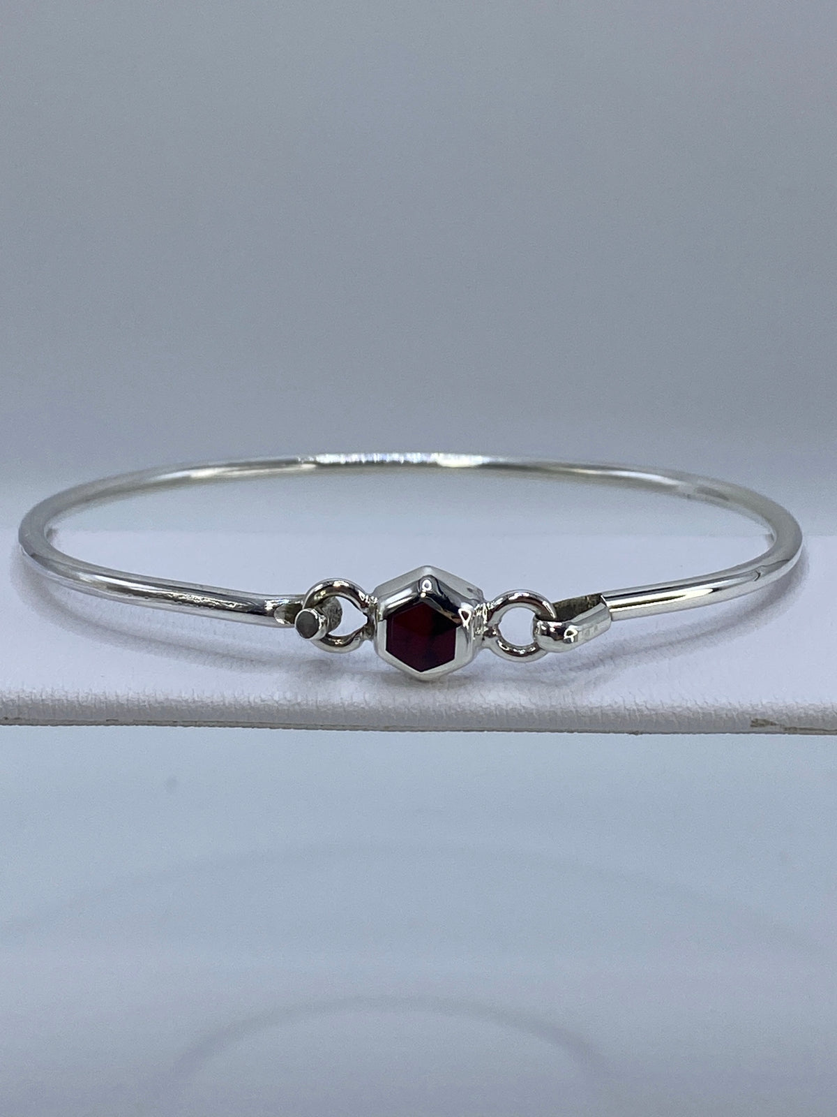 Brazalete de plata rígido con coral rojo engastado en el centro, visto de frente sobre tela blanca