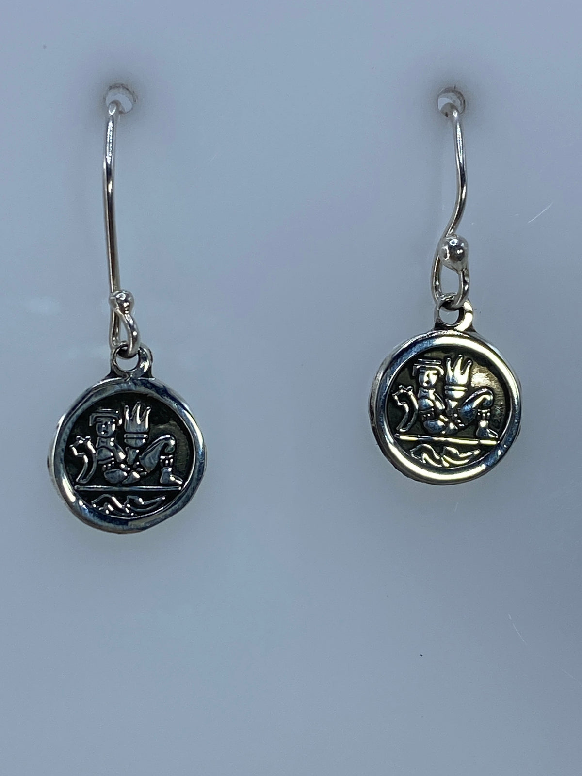 Par de aretes de plata en repujado con motivo prehispánico, vista frontal del diseño ritual