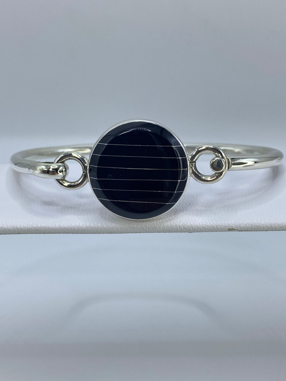 Brazalete de plata rígido con onix negro pulido en centro, sobre pulsera blanca