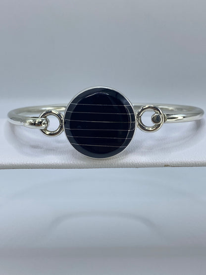 Brazalete de plata rígido con onix negro pulido en centro, sobre pulsera blanca