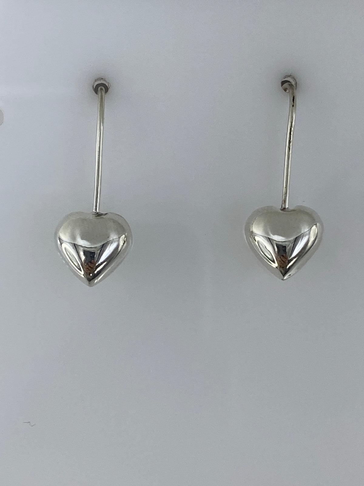 Par de aretes de plata con forma de corazón pulido, gancho plateado, sobre fondo blanco
