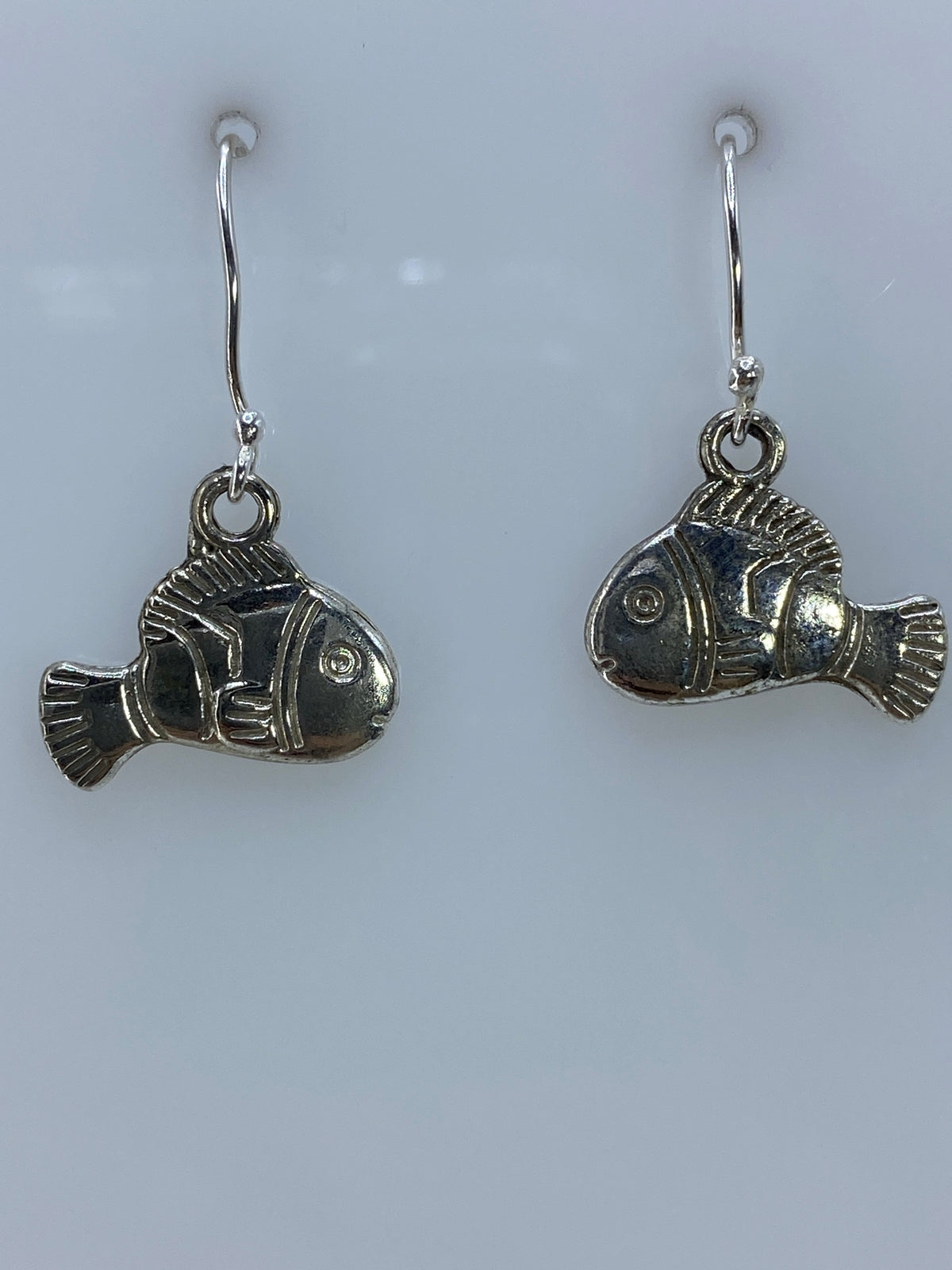 Aretes de plata en forma de pececillo con técnica de repujado, colgando de ganchos de plata