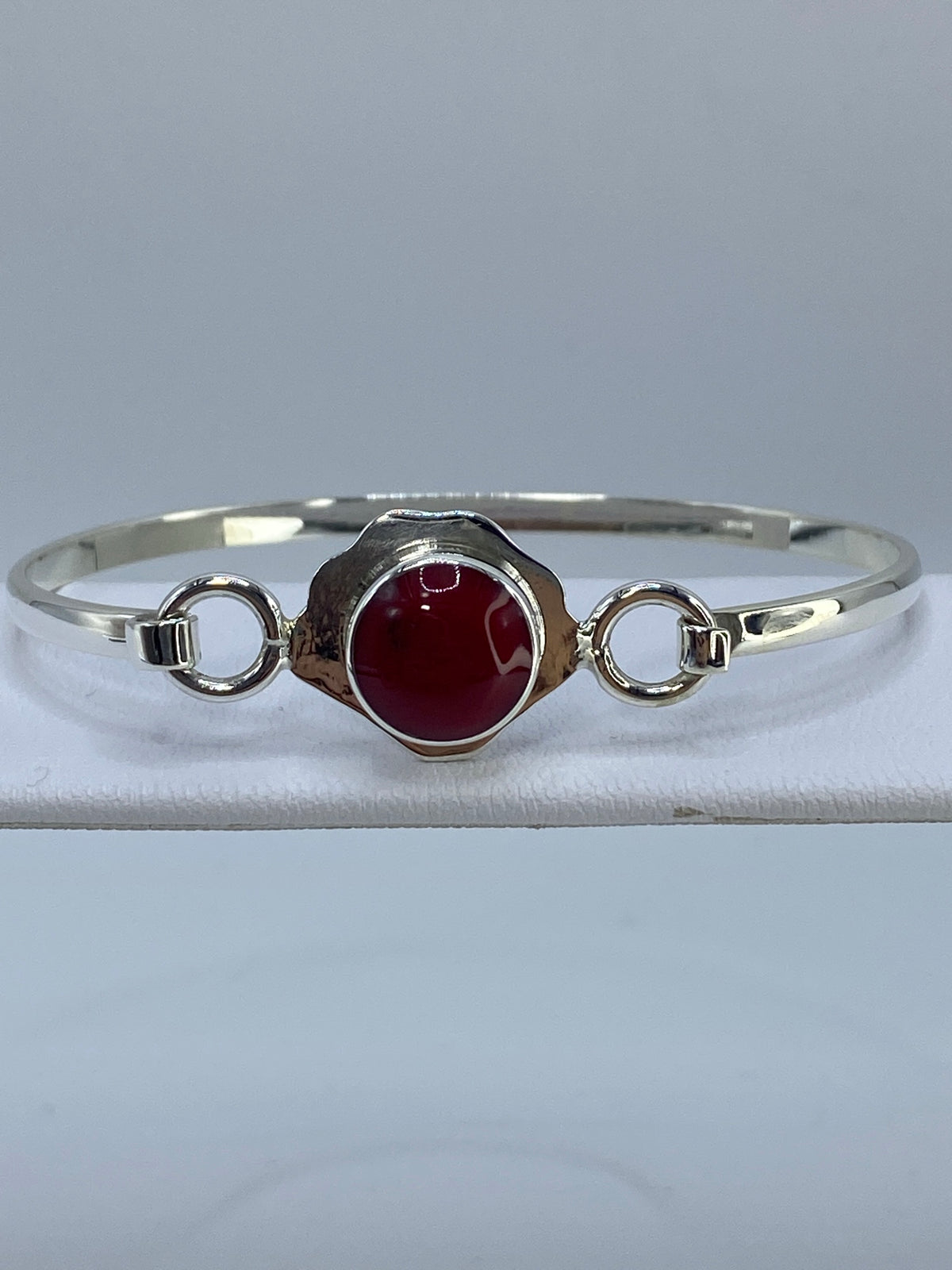 Brazalete de plata rígido tipo puño con coral rojo engastado, vista frontal sobre fondo gris
